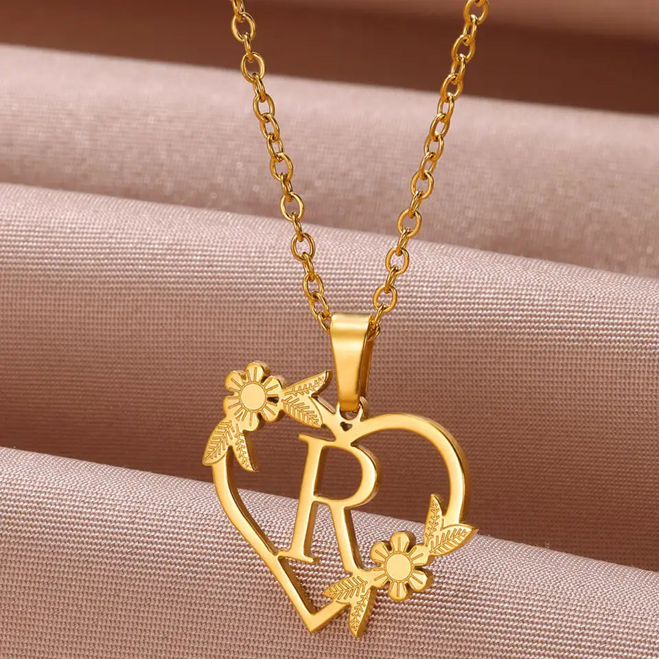 Collar dorado con dije de iniciales dentro de un corazón decorado