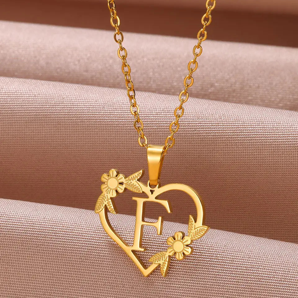 Collar dorado con dije de iniciales dentro de un corazón decorado